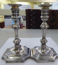 A pair of Georgian style loaded silver candlesticks of square outline, the knopped stems on incurved
