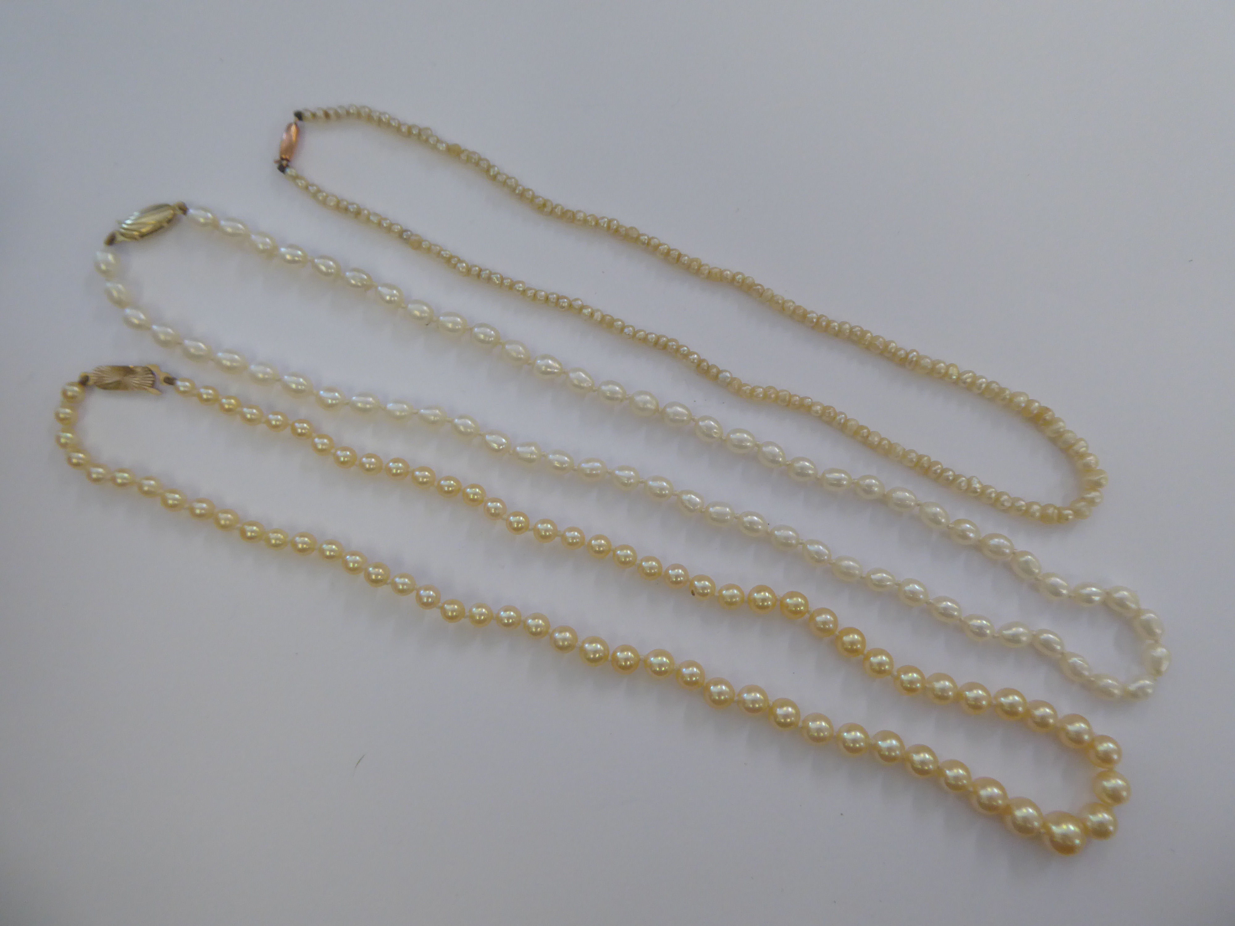 Three single strand pearl necklaces, each on a yellow metal clasp