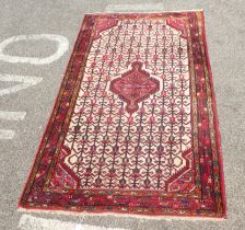A Persian rug with a central motif, bordered by repeating stylised designs, on a multi-coloured