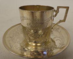 A Continental silver coloured metal coffee cup and saucer, engraved with floral and scrolled
