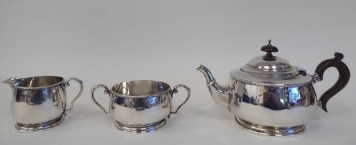 A three piece spot-hammered silver tea set with cast bead bordered decoration  comprising a round