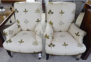 A pair of late Victorian easy chairs, each upholstered in cream leaf design fabric, raised on turned