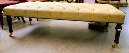 A modern footstool with a cream coloured faux hide button upholstered top, raised on turned,