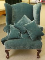 A 20thC Georgian style wingback chair with scrolled arms, upholstered in crushed turquoise