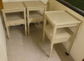 A set of three modern cream painted bedside tables, each with a drawer, raised on square, tapered