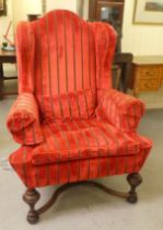 A 20thC Georgian style wingback chair with scrolled arms, upholstered in striped, crushed red and