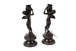 A pair of bronze candlesticks in the form of putti carrying urns.