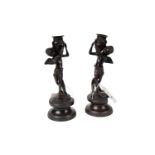 A pair of bronze candlesticks in the form of putti carrying urns.