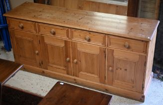 A modern pine sideboard with four drawers over four cupboards, on a plinth base, 183 cm x 49 cm x 82