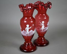 A pair of cranberry glass vases with crenellated rims and waisted stems, painted with children