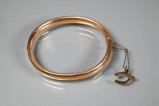 A yellow metal half hinged oval bangle with concealed clasp and safety chain, stamped 15ct, approx