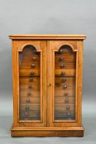 A Victorian style collector's table cabinet, the pair of arched glazed-in doors enclosing twelve