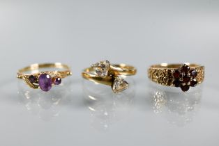 Three 9ct yellow gold rings - a three-stone amethyst in scroll setting, garnet cluster and two stone
