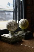 A pair of large weathered old cast stone spherical finials, raised on square socle bases, 40 cm x 40