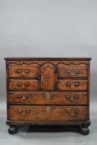 An 18th century oak chest, the wavy frieze over a centre cupboard flanked by short two tier drawers,