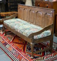A George III oak settle, the panelled back with shapes arms over a wood slat seat (and loose cushion