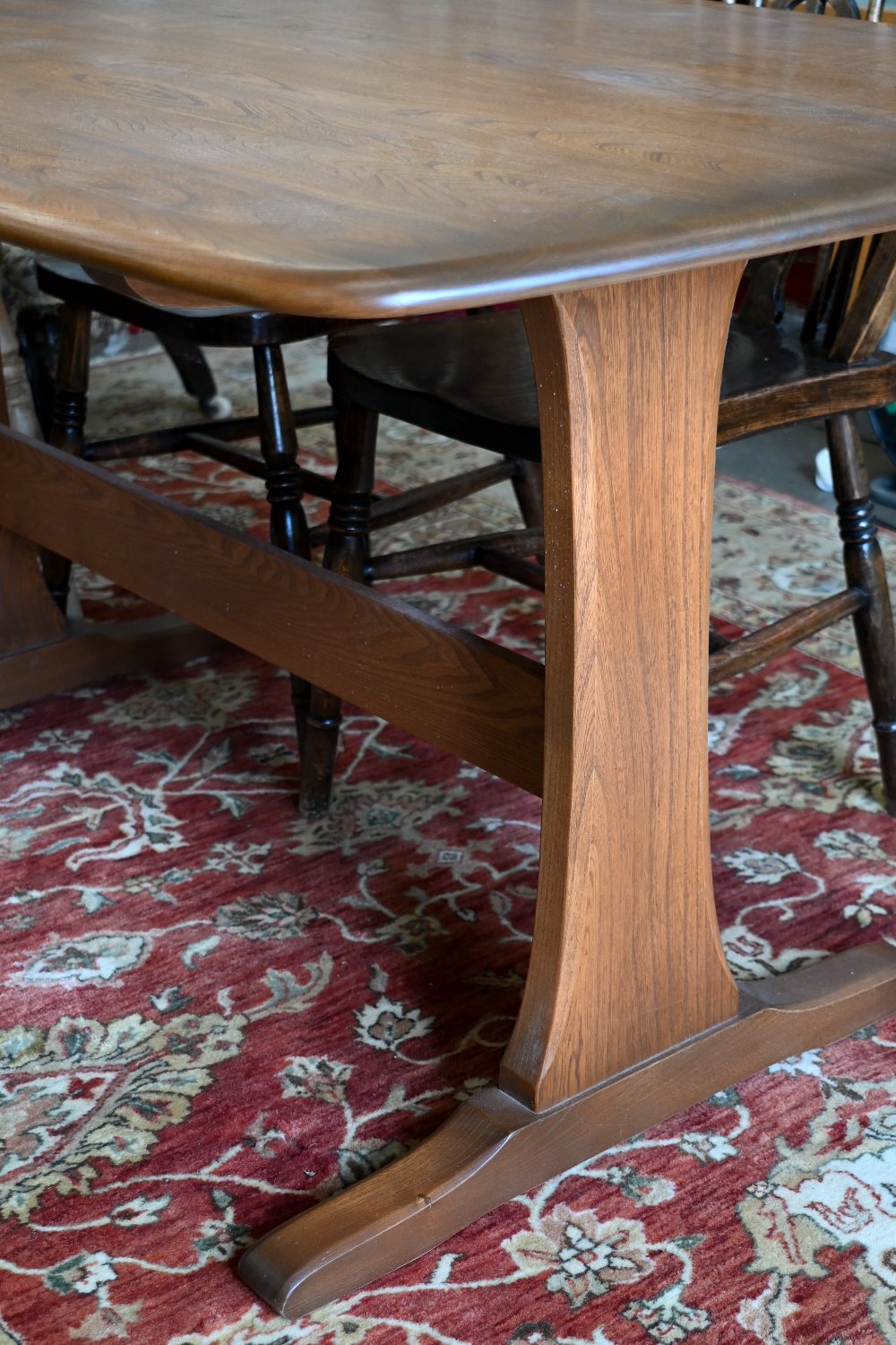 An Ercol dark elm dining table on twin-trestle supports united by the central stretcher, 150 cm x 84 - Image 2 of 3