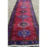 A North West Persian runner, geometric medallions on red ground with navy borders 388 x 108cm