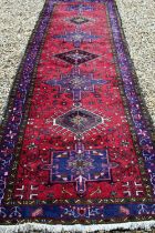 A North West Persian runner, geometric medallions on red ground with navy borders 388 x 108cm