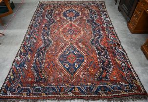 A Persian Shiraz carpet with navy medallions on terracotta ground, 310 x 210 cm