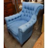 A deep-buttoned armchair covered in blue twill fabric, on tapering supports