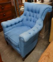A deep-buttoned armchair covered in blue twill fabric, on tapering supports