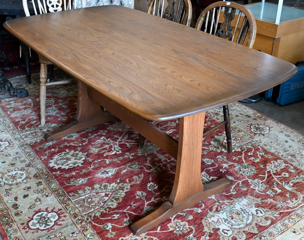 An Ercol dark elm dining table on twin-trestle supports united by the central stretcher, 150 cm x 84