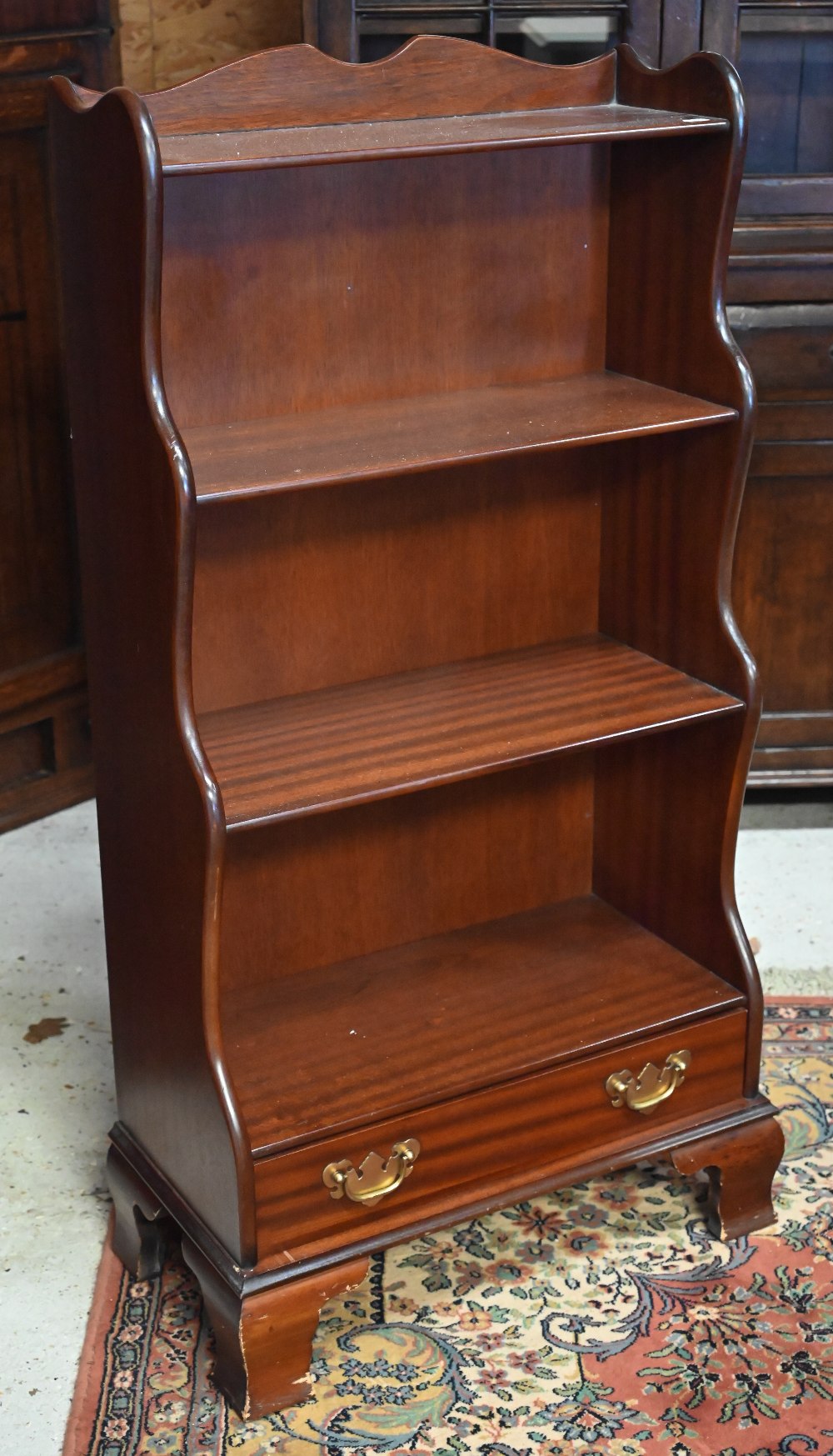 A reproduction mahogany waterfall bookcase with single drawer standing on bracket feet, 58 x 30 x