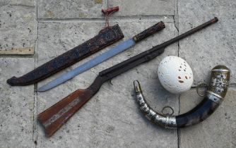 An ornamental powder horn with metal mounts, a carved ostrich egg, a Tribal machete and an air rifle