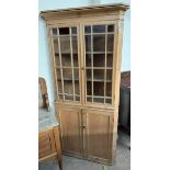 A 19th century pine standing corner cupboard with a pair of glazed doors with glazing bars the base