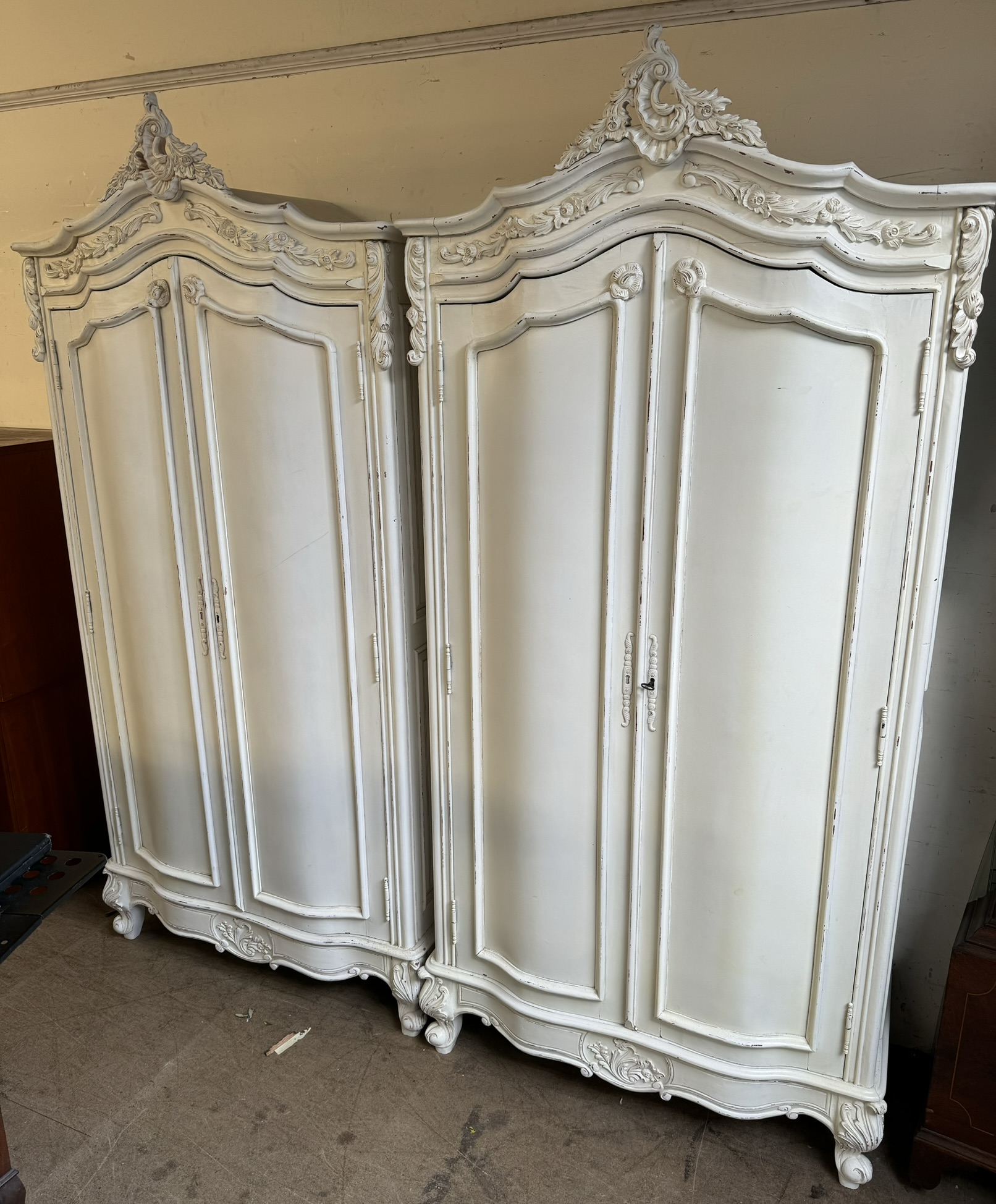 A pair of cream painted armoires with carved cresting and a pair of cupboard doors on leaf carved