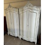 A pair of cream painted armoires with carved cresting and a pair of cupboard doors on leaf carved