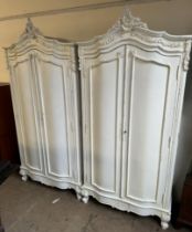 A pair of cream painted armoires with carved cresting and a pair of cupboard doors on leaf carved
