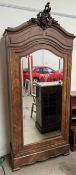 A French walnut armoire with a carved cresting rail above a mirrored door, on a shaped base,