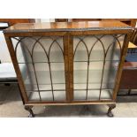 A 20th century walnut display cabinet with a rectangular top with a leaf carved edge above a pair