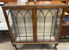 A 20th century walnut display cabinet with a rectangular top with a leaf carved edge above a pair