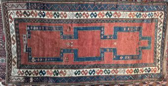 A large rug with a central red ground and a blue internal track with stylised animals to multiple