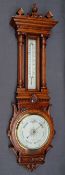 An Edwardian oak aneroid barometer with a carved and turned cresting rail above a mercury
