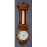 An Edwardian oak aneroid barometer with a carved and turned cresting rail above a mercury