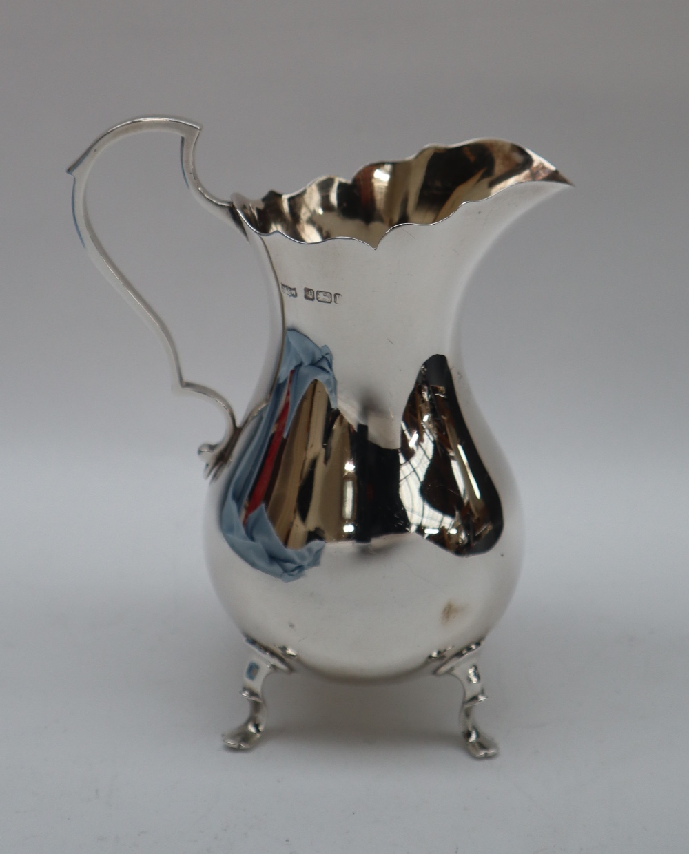 An Edward VII silver cream jug of baluster form with a scrolling handle on four feet, Sheffield,