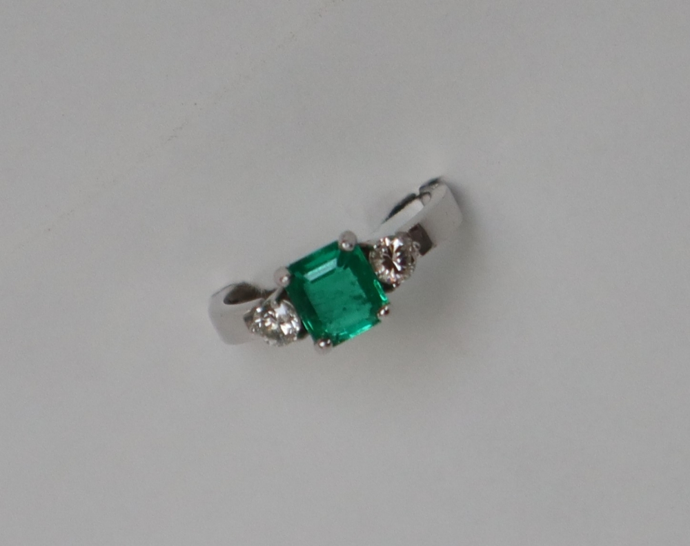 An emerald and diamond ring set with a central emerald cut emerald approximately 6mm x 5mm,