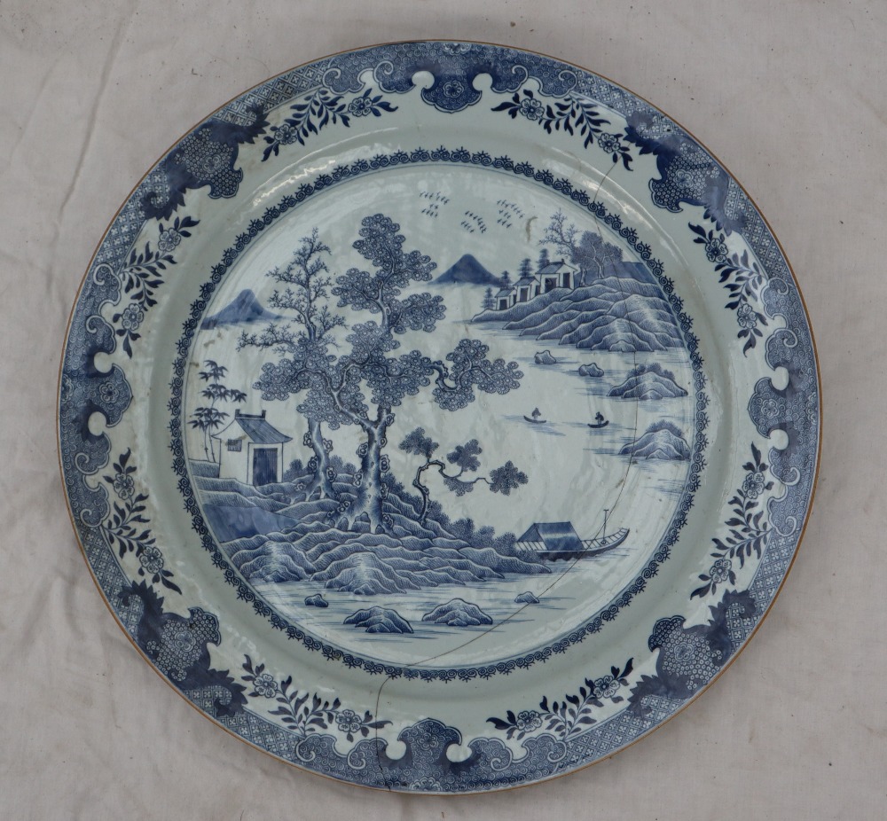 A large Chinese blue and white porcelain charger, decorated with cottages and trees on a river,