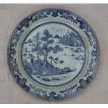 A large Chinese blue and white porcelain charger, decorated with cottages and trees on a river,