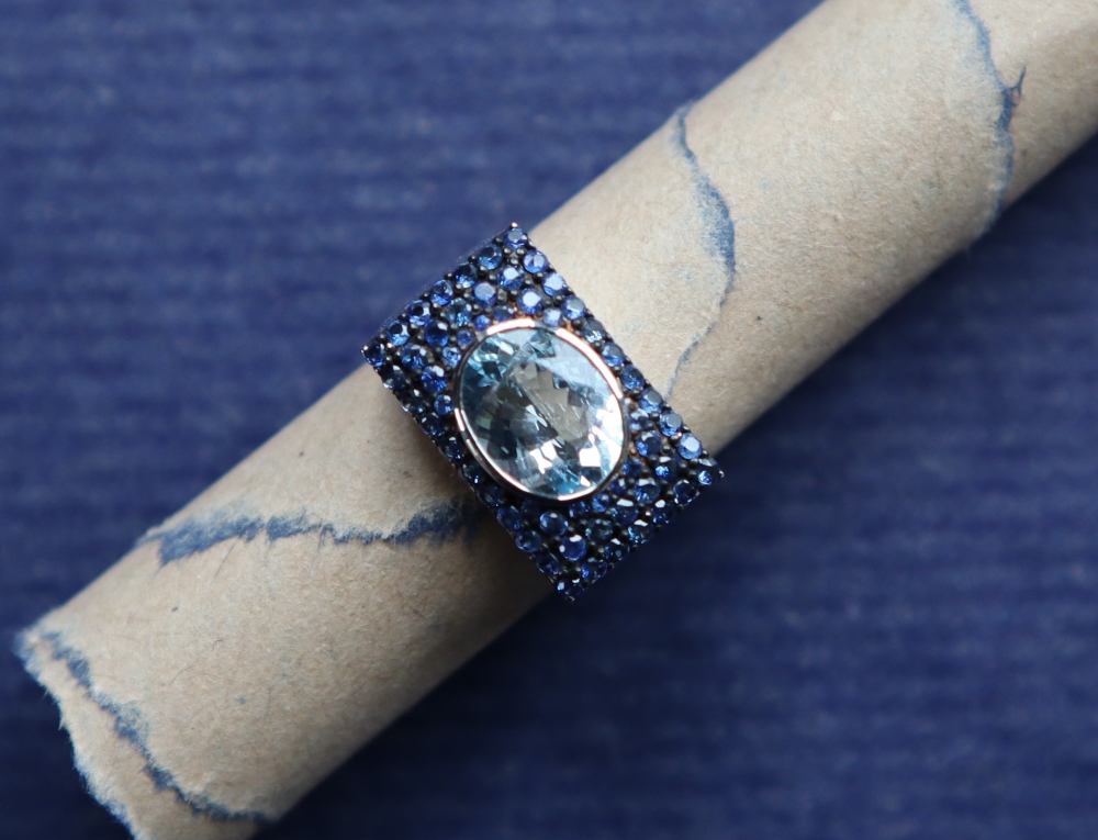 An Art Deco style aquamarine and sapphire dress ring with a rub over set oval aquamarine