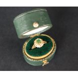 An emerald and diamond ring set with a central circular faceted emerald surrounded by two tiers of