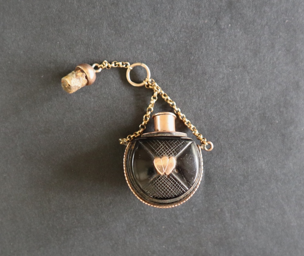 A small scent bottle the ebonised body inset and mounted in yellow metal on a chain