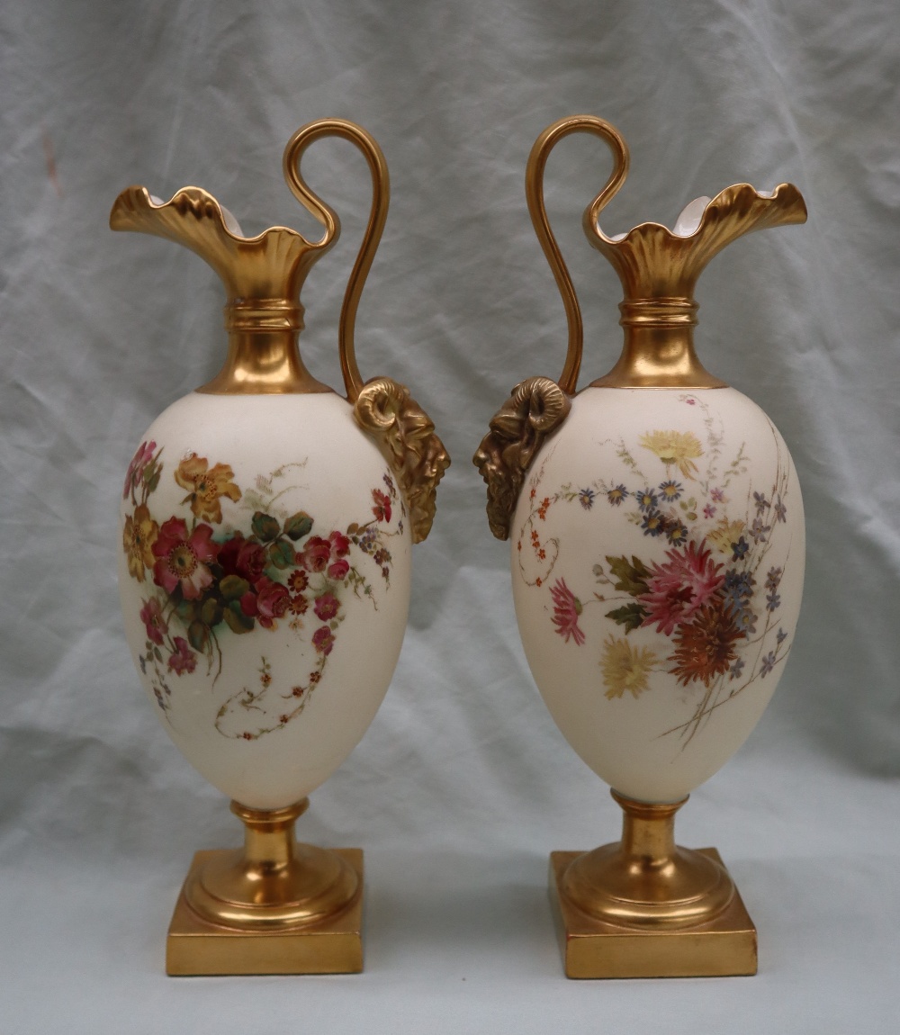 A pair of Royal Worcester porcelain ewers with wavy spout, mask terminal handles,