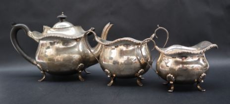 A George V silver three piece tea service with a gadrooned edge and bulbous body on four feet,