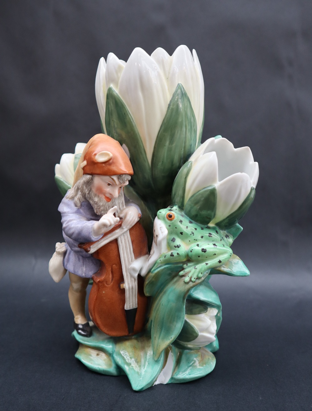 A continental porcelain triple lily vase moulded with a bearded sprite playing a cello with the