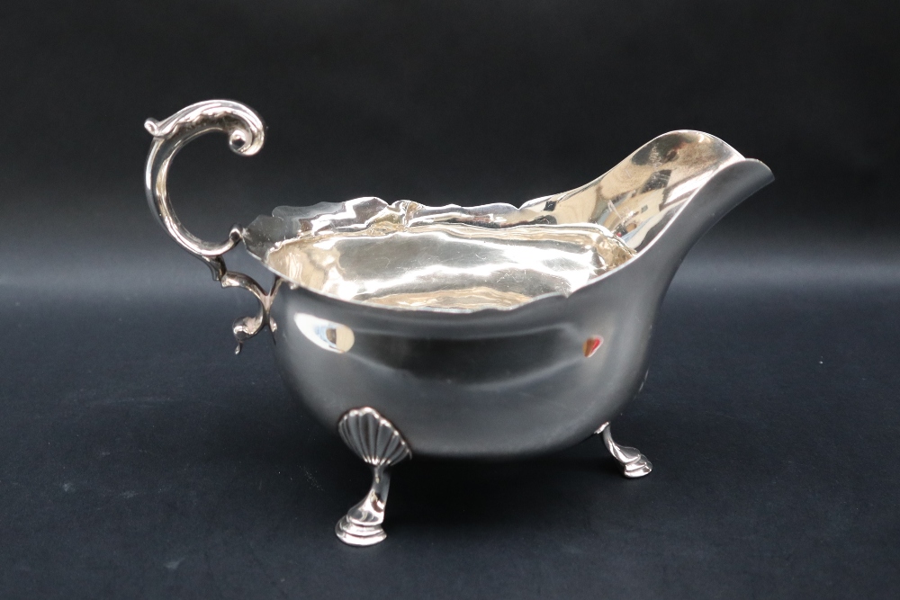 A Victorian silver sauce boat with a flared rim and scrolling handle on three shell capped legs and